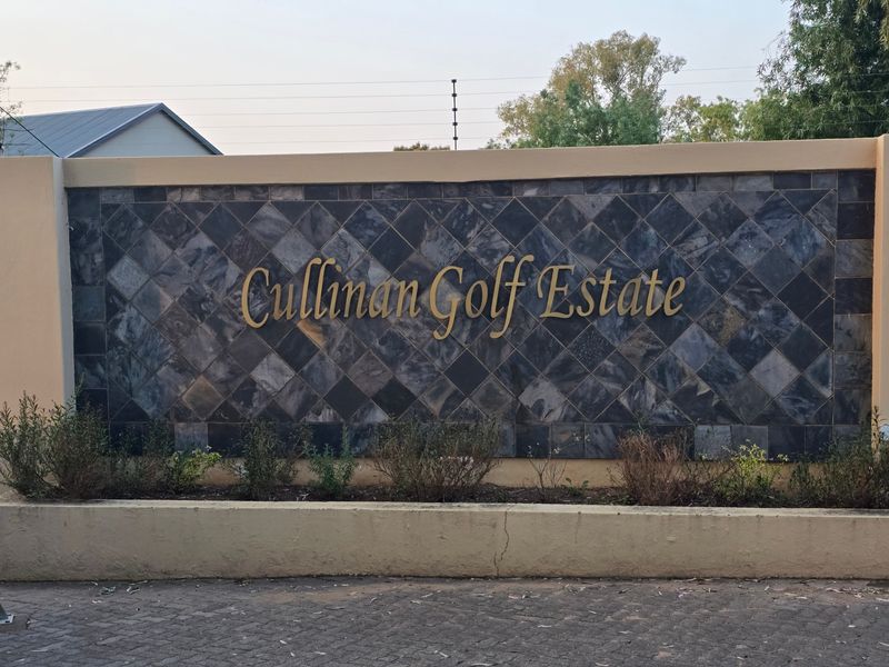 Entrance signage wall for Cullinan Golf Estate featuring stone cladding, electric fencing, and a paved driveway approach.