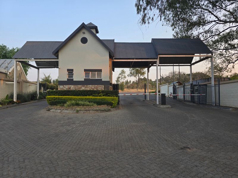 A well-maintained residential estate security gatehouse featuring a paved driveway, boom gate access, and stone-clad architectural detailing.