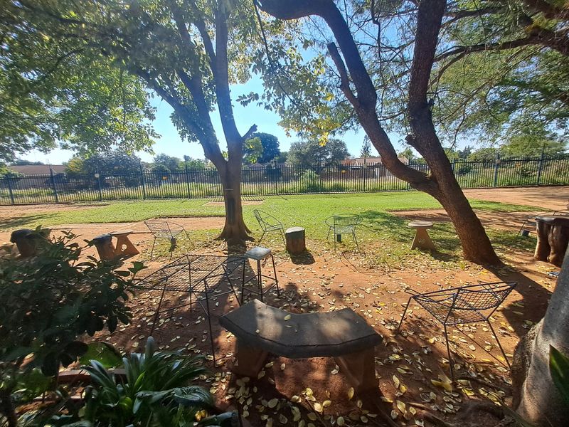 A spacious garden area featuring mature trees, a stone bench, and secure metal perimeter fencing, offering a natural outdoor setting.