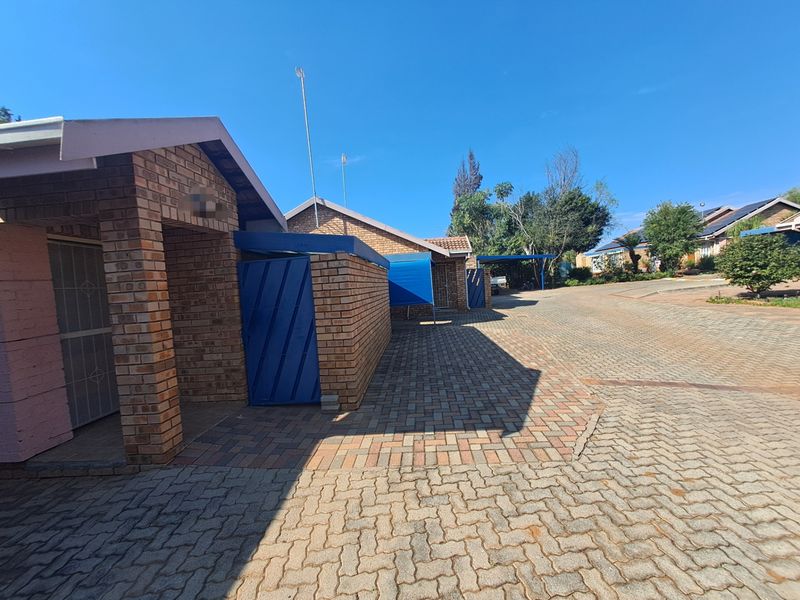 Exterior view of a townhouse complex featuring face brick construction, paved driveway access, and secure gated entry points.
