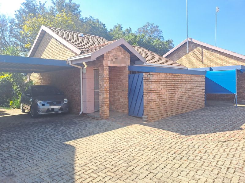 Front exterior view of a facebrick townhouse featuring a paved driveway, covered carport, and secure entrance area.