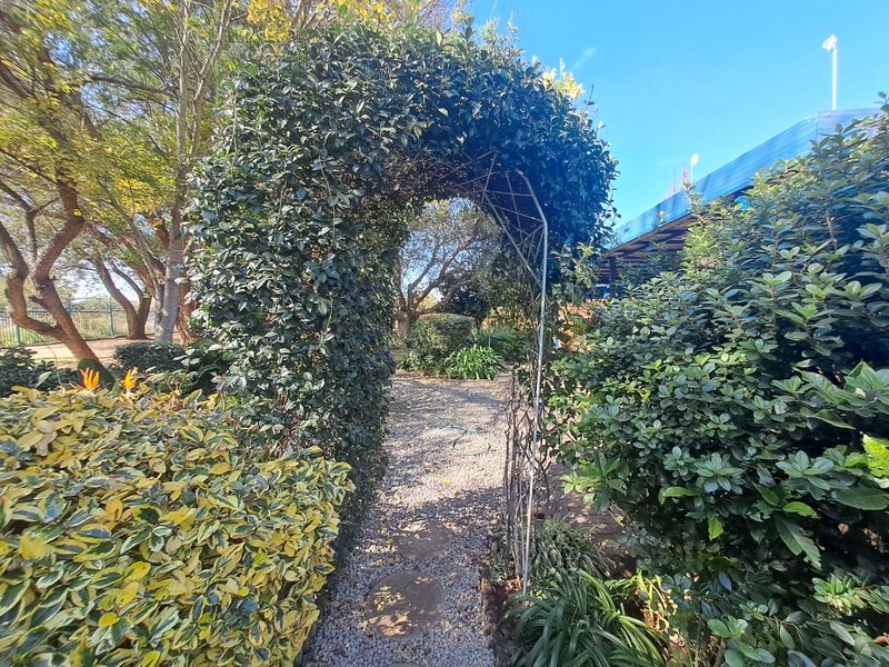 A well-established garden featuring a metal archway over a gravel pathway with mature shrubs and stepping stones.