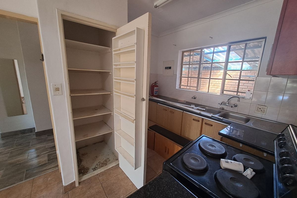 A functional kitchen featuring built-in cabinetry, a pantry with shelving, a double sink, and an electric stove, requiring cosmetic updates to modernize the space.