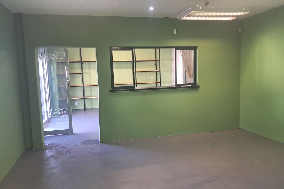 An empty commercial office space featuring green painted walls, a service window, built-in shelving, and a glass entrance door.