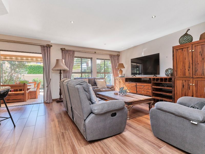 Spacious open-plan living area featuring wood-look tile flooring, recessed lighting, and seamless access to an outdoor patio through large sliding glass doors.