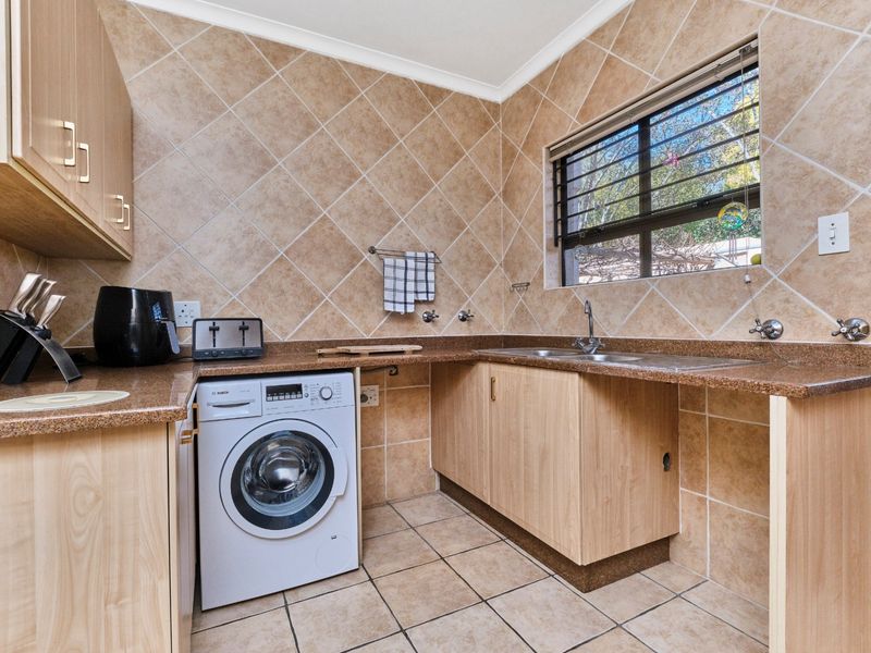 Functional laundry area featuring built-in light wood cabinetry, granite countertops, a double sink, and tiled finishes throughout.