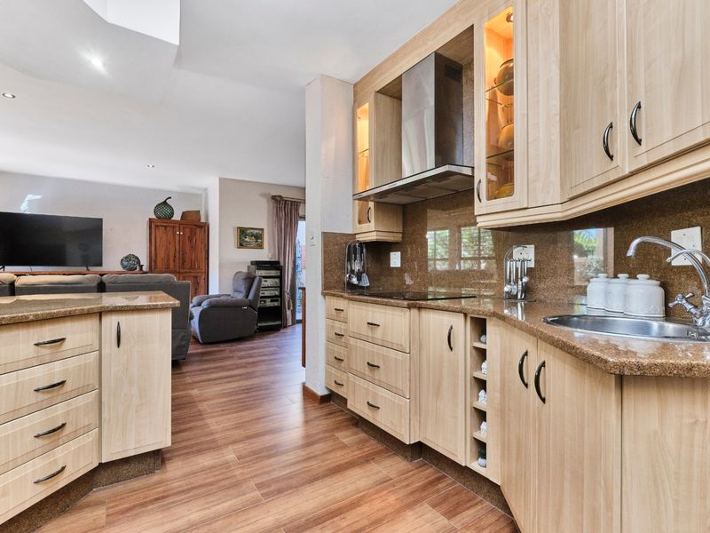 Open-plan kitchen featuring light wood cabinetry, granite countertops, and integrated appliances, flowing seamlessly into the adjacent living area with laminate flooring.