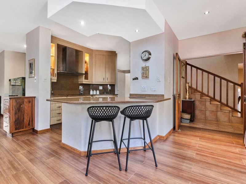 Open plan kitchen featuring granite countertops, wooden cabinetry, and an integrated breakfast nook, seamlessly flowing into the living area with staircase access.