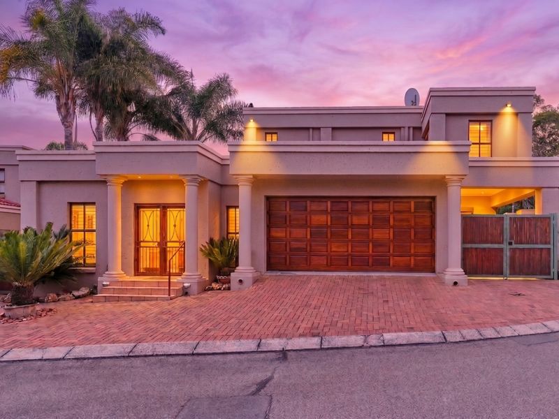 Front elevation of a modern cluster home featuring a paved driveway, double wooden garage door, and decorative columns at the entrance.