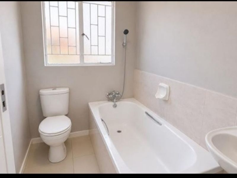 A clean, functional bathroom featuring a white bathtub, toilet, and basin with neutral wall and floor tiling.