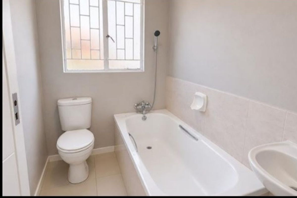A clean, functional bathroom featuring a white bathtub, toilet, and basin with neutral wall and floor tiling.