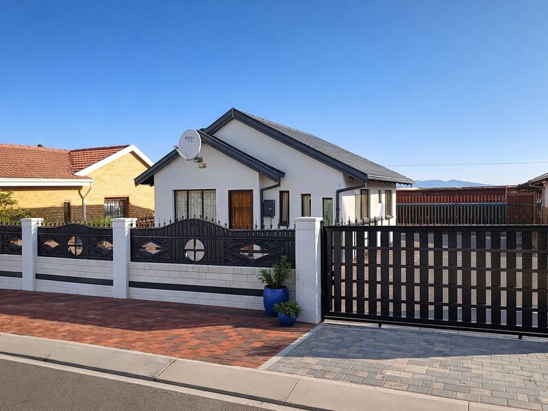 Front view of a well-maintained detached house featuring a paved driveway, secure metal gate, and decorative boundary wall.