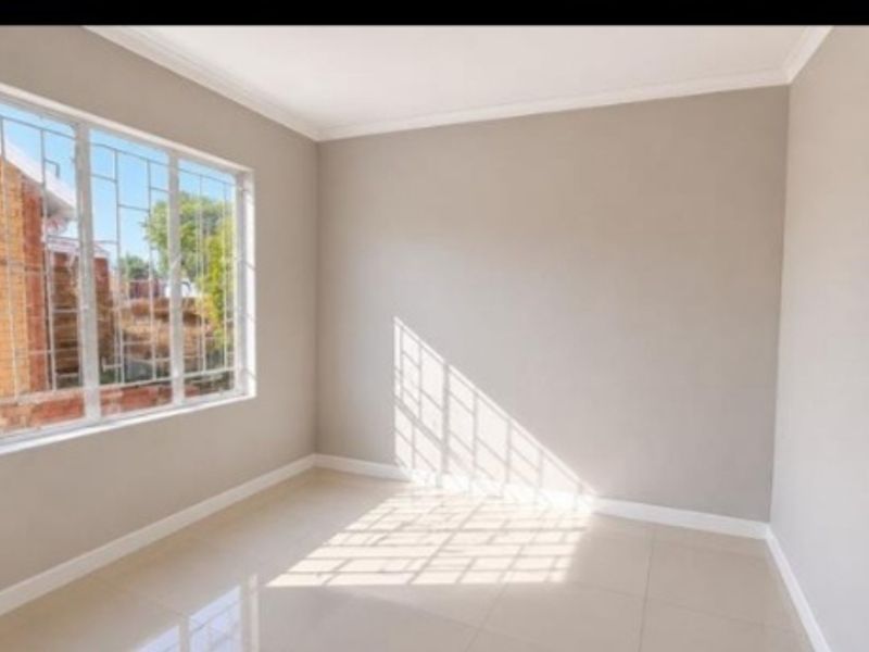 A bright, empty bedroom featuring neutral wall paint, tiled flooring, and a window fitted with security bars.