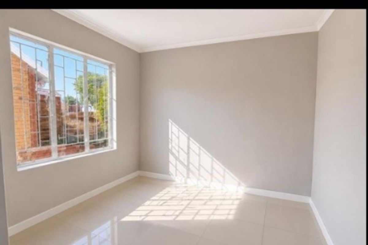 A bright, empty bedroom featuring neutral wall paint, tiled flooring, and a window fitted with security bars.