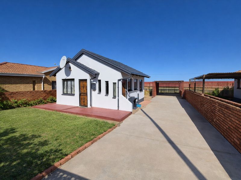 Front view of a detached house featuring a concrete driveway, brick boundary walls, and a well-maintained lawn area.