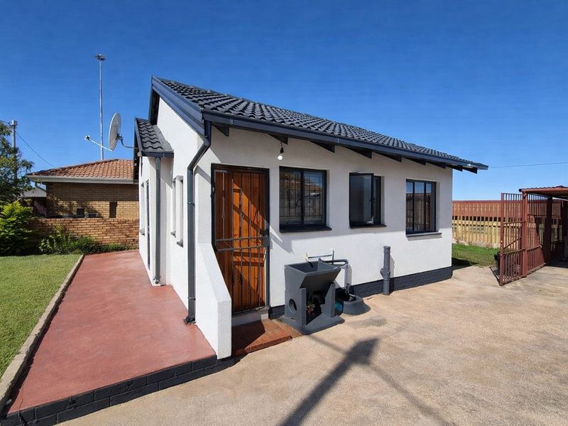Rear view of a well-maintained detached structure featuring a tiled roof, security gates, and an external wash basin on a concrete driveway.
