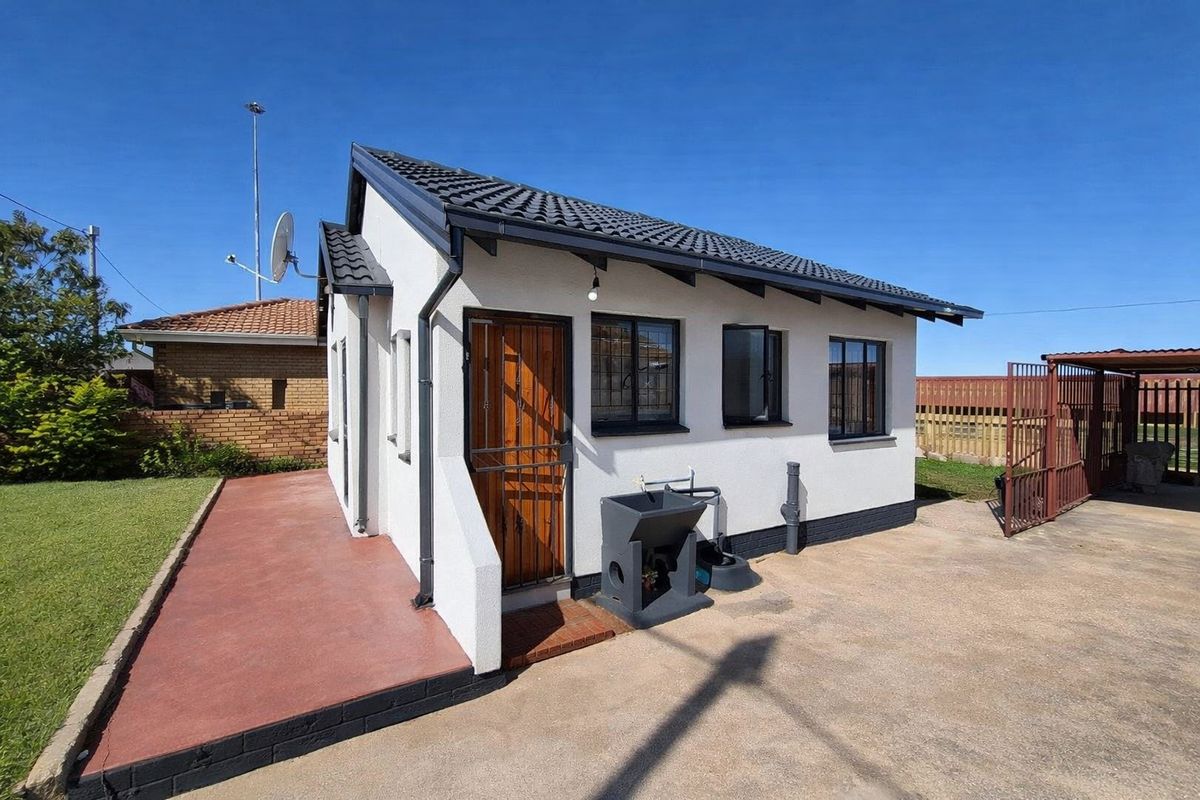 Rear view of a well-maintained detached structure featuring a tiled roof, security gates, and an external wash basin on a concrete driveway.