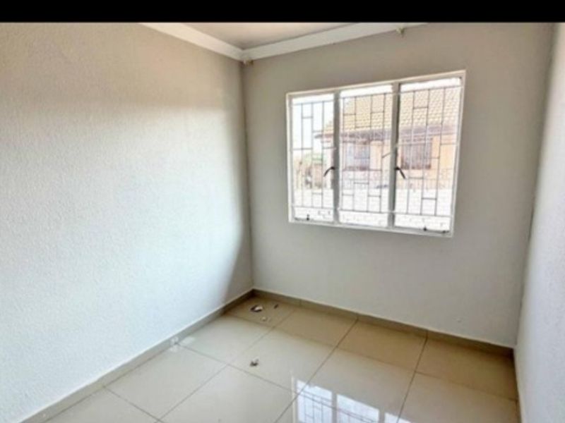 A clean, empty bedroom featuring neutral walls, tiled flooring, and a window fitted with security bars.