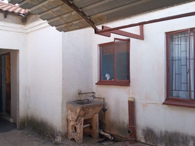 Rear exterior area featuring a concrete utility sink, metal awning, and security-barred windows, showing signs of significant wear and exterior wall staining.