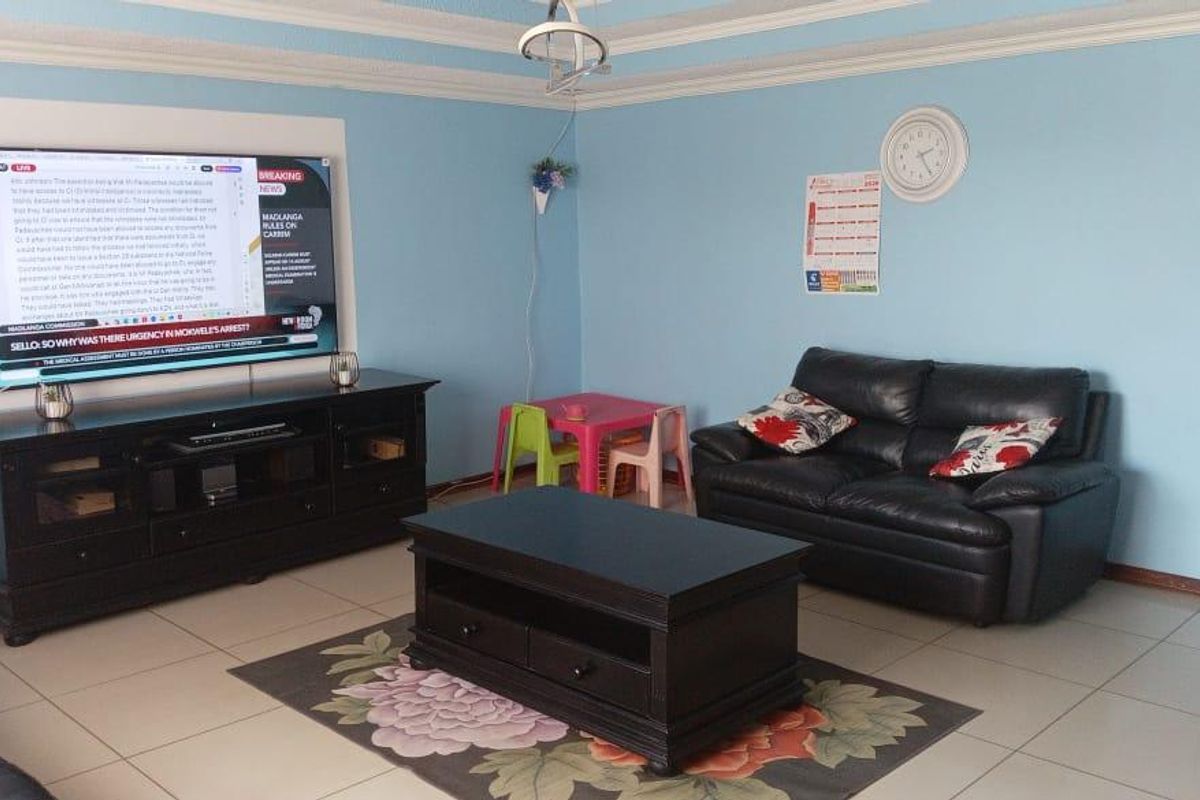 A living room featuring tiled flooring, decorative ceiling cornices, and a wall-mounted television setup.