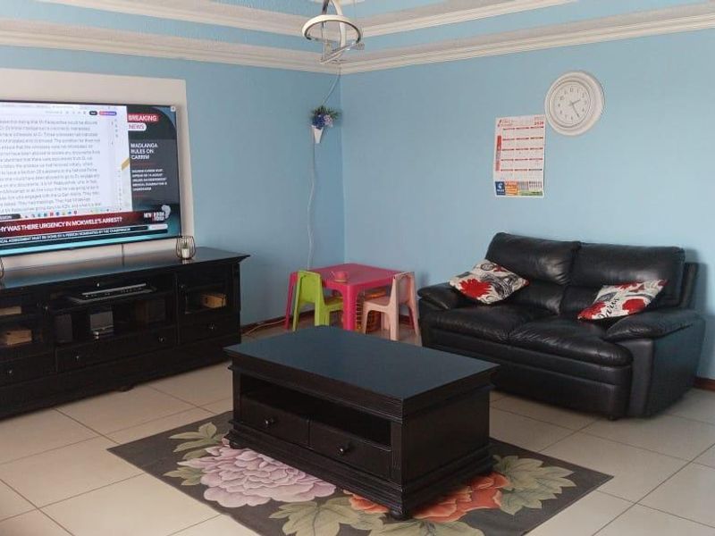 A living room featuring tiled flooring, decorative ceiling cornices, and a wall-mounted television setup.