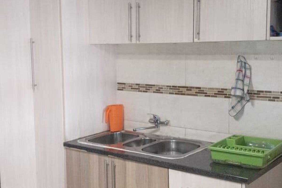 Compact kitchen featuring light wood-grain cabinetry, granite countertops, a double stainless steel sink, and neutral tiled flooring.