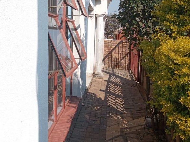 A side walkway featuring paved flooring, classical architectural columns, and top-hung windows along the exterior wall of the property.
