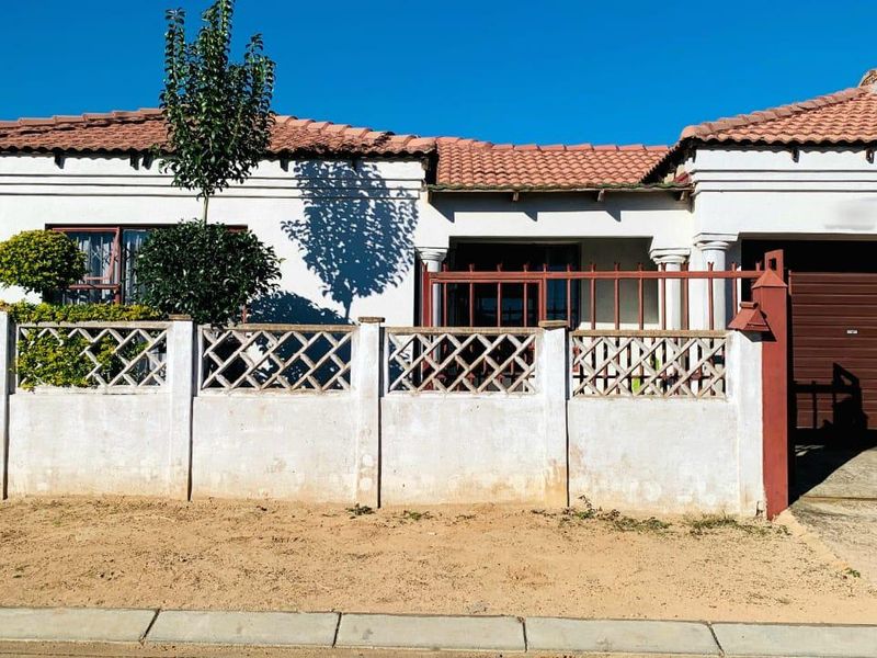 Front elevation of a single-story house featuring a tiled roof, integrated garage, and a concrete boundary wall with decorative lattice panels.