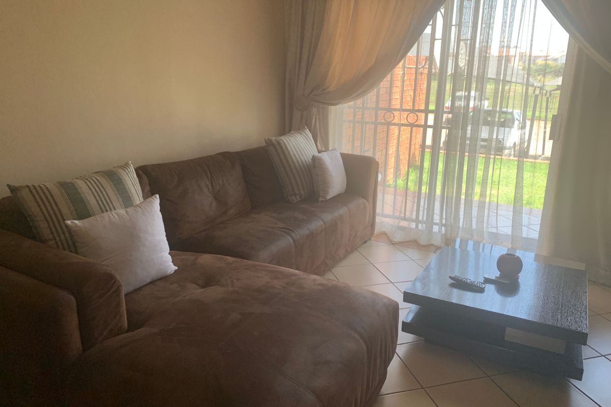 A comfortable living room featuring tiled flooring and a sliding glass door with a security gate, providing direct access to the outdoor area.