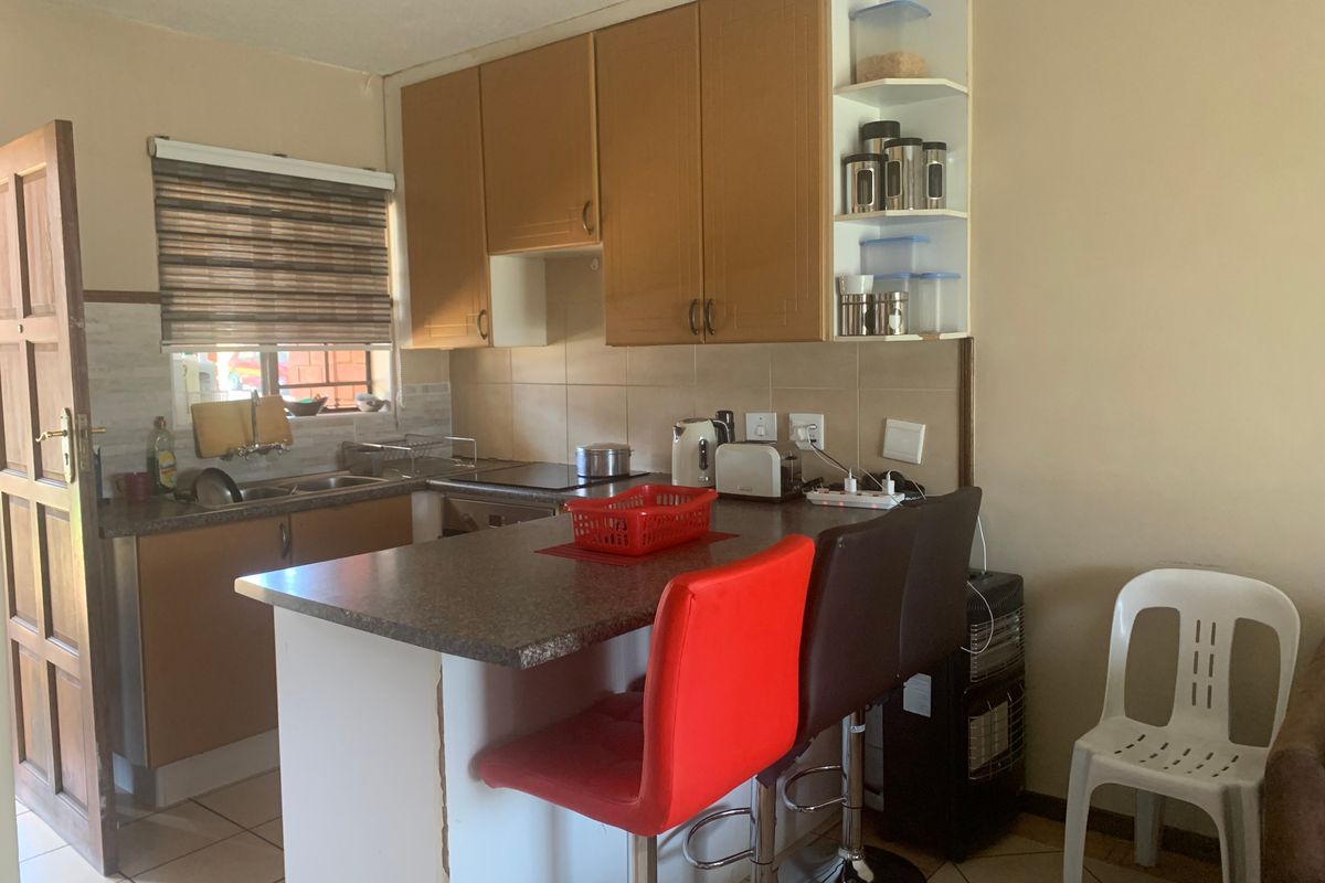 A compact kitchen featuring laminate cabinetry, a breakfast bar, and tiled backsplash, offering a functional layout with potential for modern cosmetic updates.
