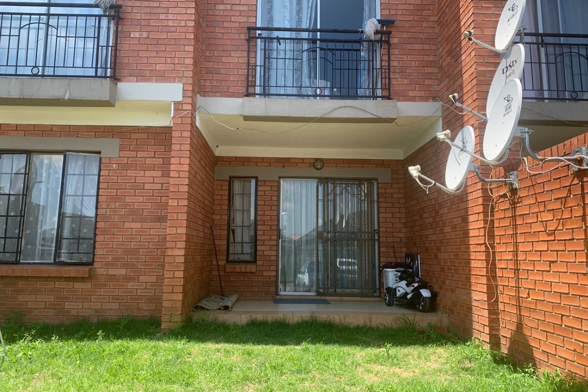 Rear view of a face brick apartment building featuring a ground floor patio with security gate and an upper level balcony with metal railings.