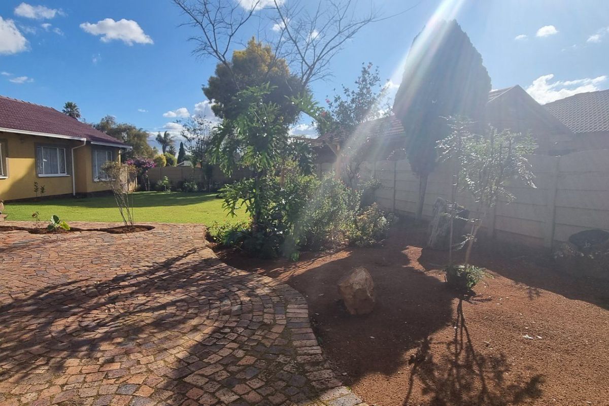 A spacious rear garden featuring a paved patio area, well-maintained lawn, and secure precast concrete boundary walling.