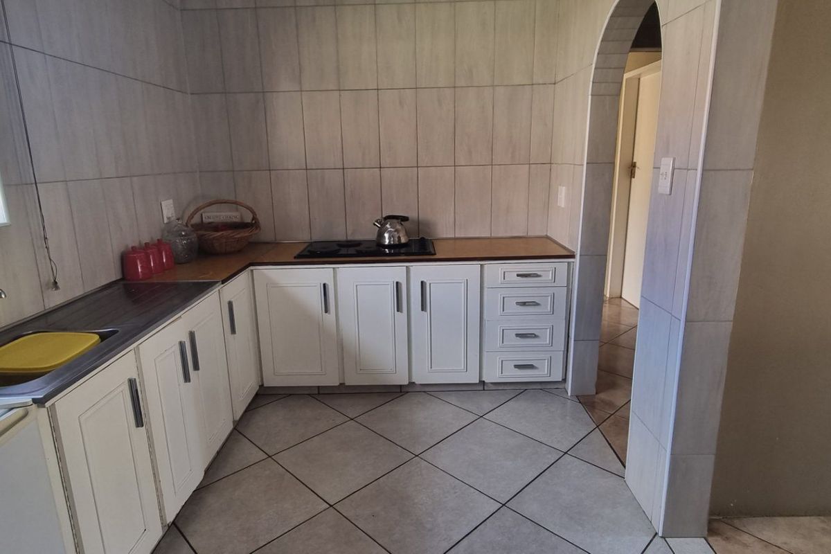 Functional kitchen featuring white cabinetry, laminate countertops, built-in hob, and tiled finishes, connected to the rest of the home via an arched doorway.