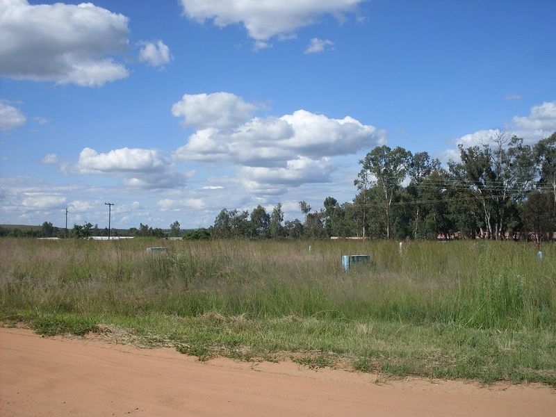 A view of a vacant residential plot featuring natural grass cover, utility infrastructure, and direct access from an unpaved road.