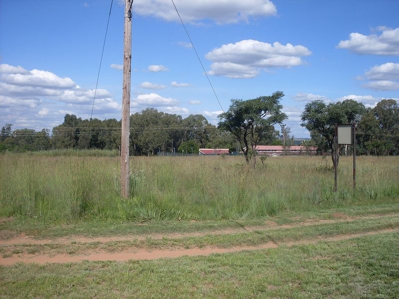 A view of a vacant residential plot featuring natural grass, a utility pole, and a signage post.
