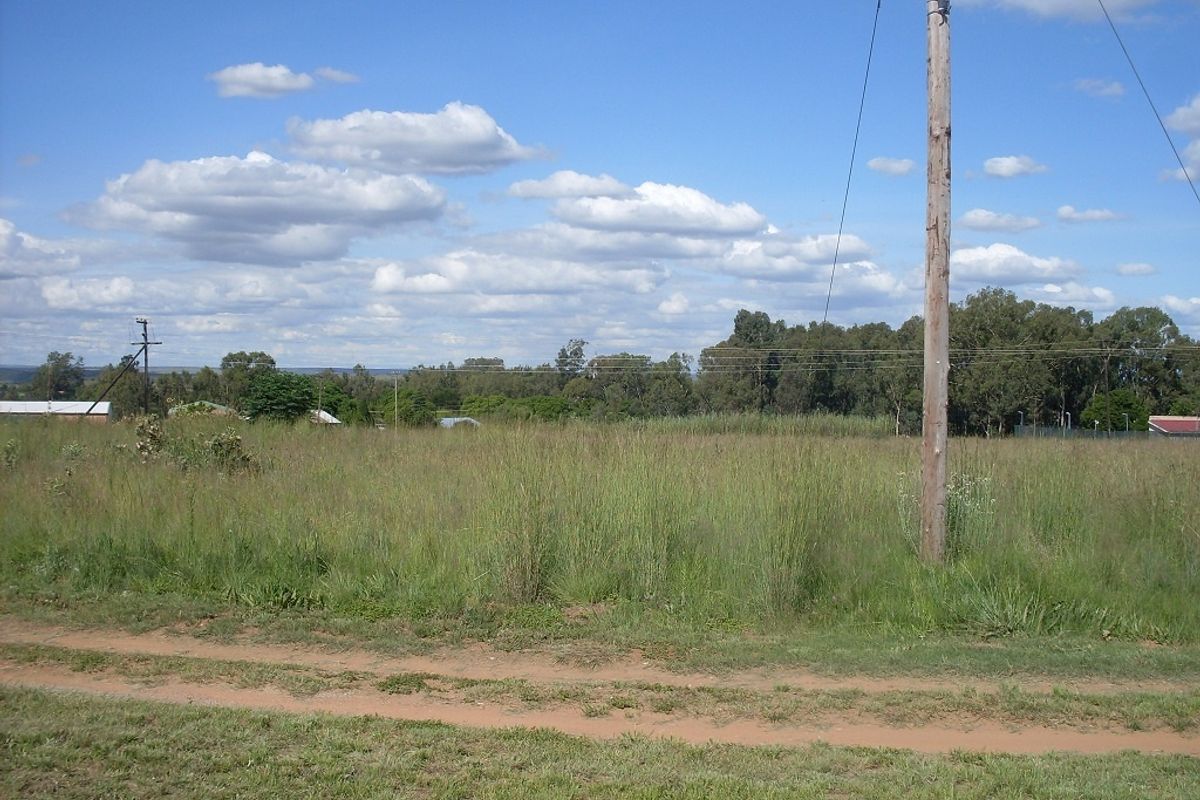 A view of a vacant residential plot featuring natural grass cover, an unpaved access path, and existing utility infrastructure.