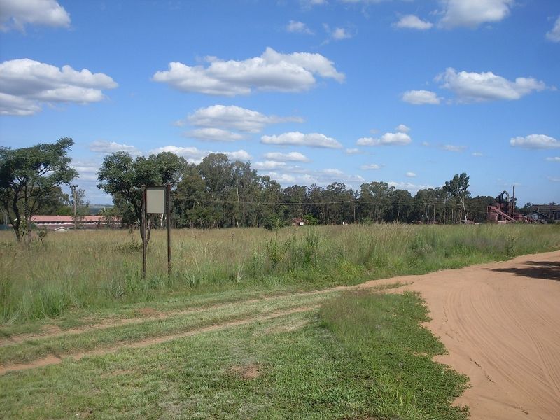 A view of a vacant residential plot featuring natural grass cover and a dirt road access point.