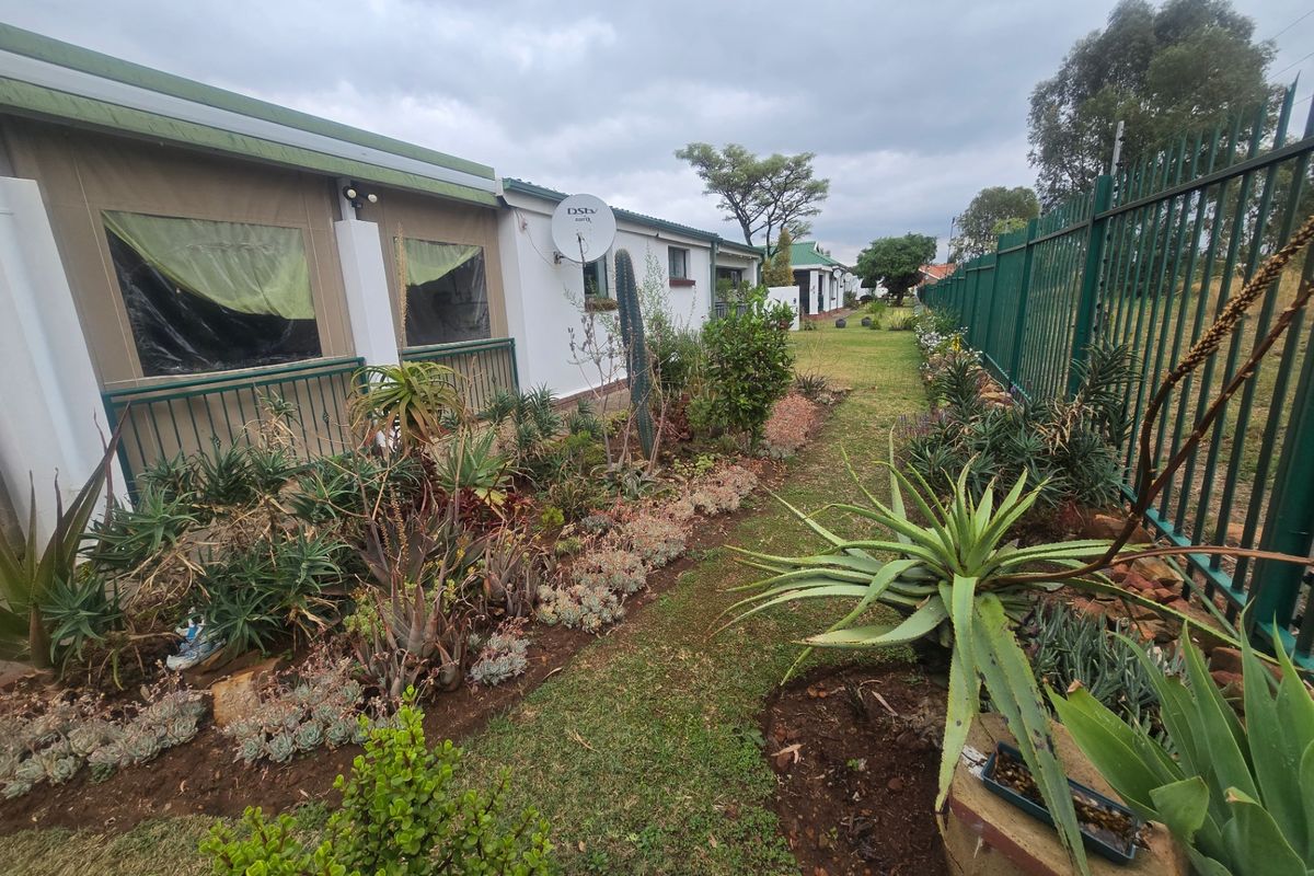 A view of the rear exterior of the townhouse, featuring a landscaped garden with established succulents and a metal perimeter fence.