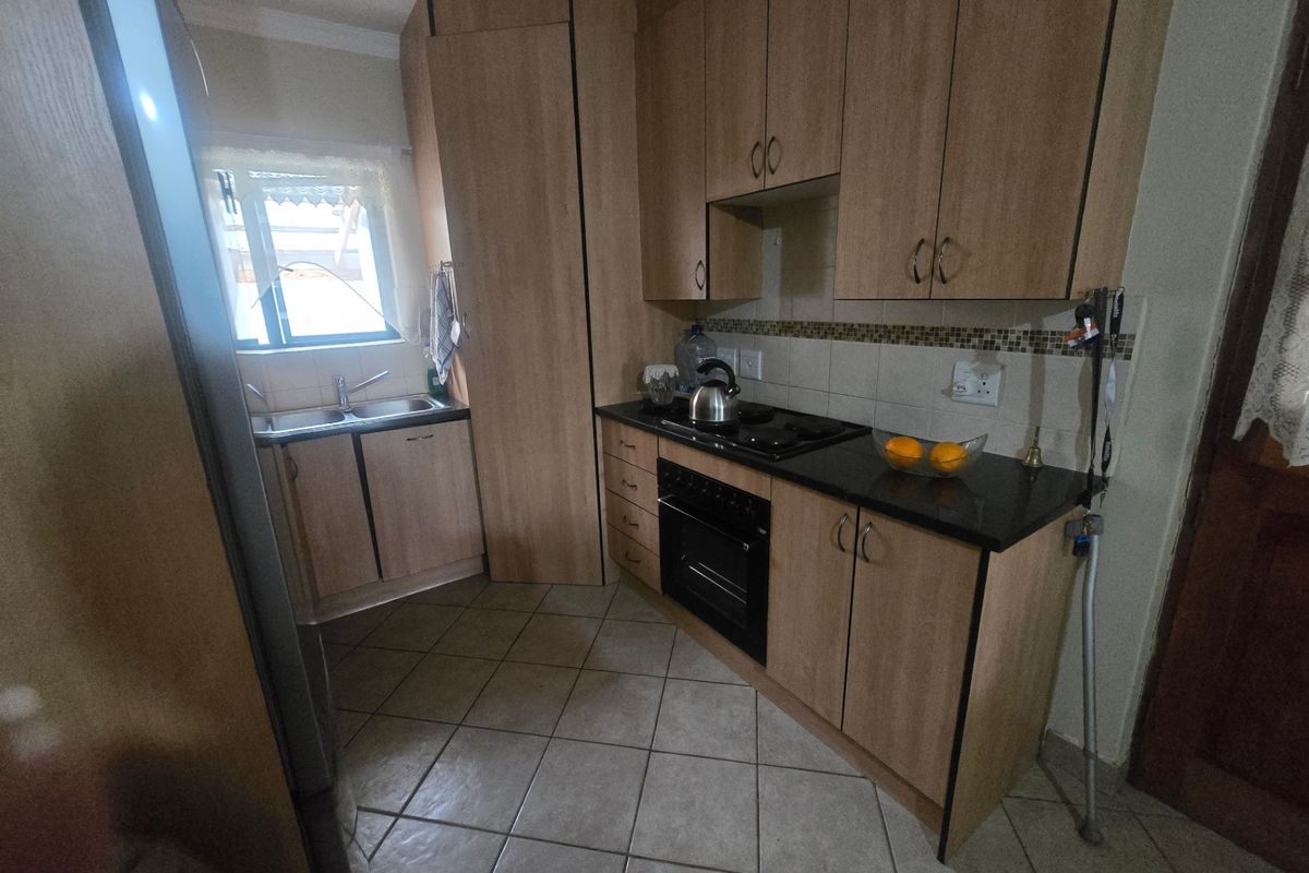 A functional kitchen featuring light wood-finish cabinetry, granite countertops, a built-in oven with gas hob, and tiled flooring.