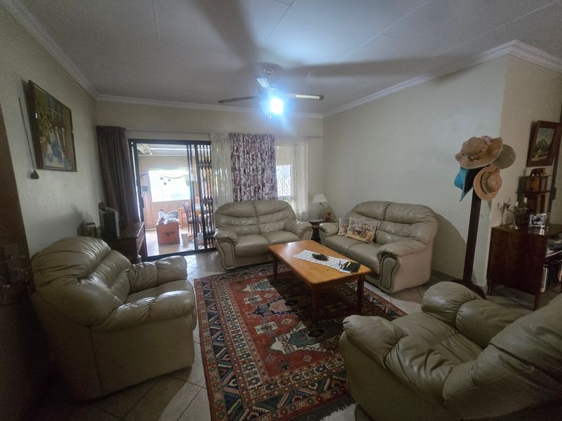 A spacious living room featuring tiled flooring, a ceiling fan, and a sliding glass door providing access to the patio area.