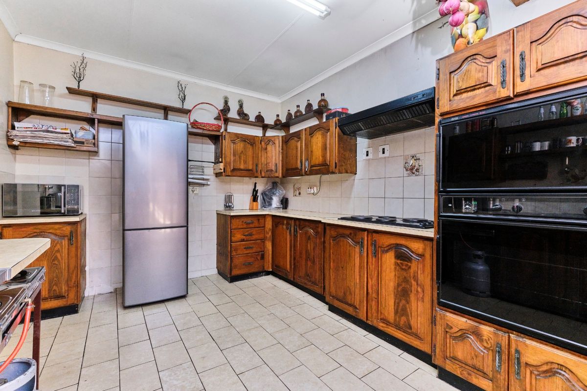 A dated kitchen featuring traditional wooden cabinetry, tiled flooring, and built-in cooking appliances, offering significant potential for a modern renovation.