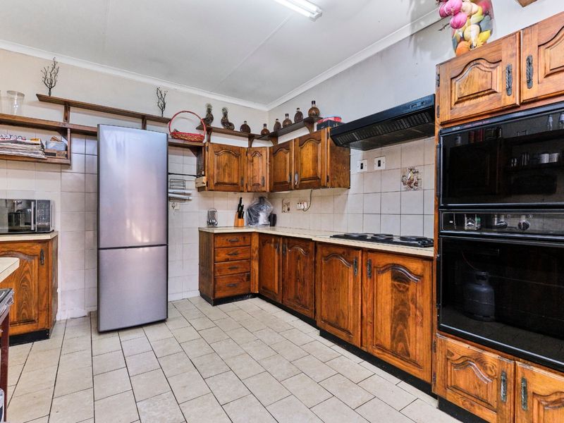 A dated kitchen featuring traditional wooden cabinetry, tiled flooring, and built-in cooking appliances, offering significant potential for a modern renovation.
