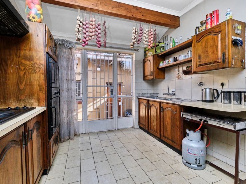A dated kitchen featuring timber cabinetry, tiled flooring, built-in oven, gas hob, and a security gate leading to an exterior area.