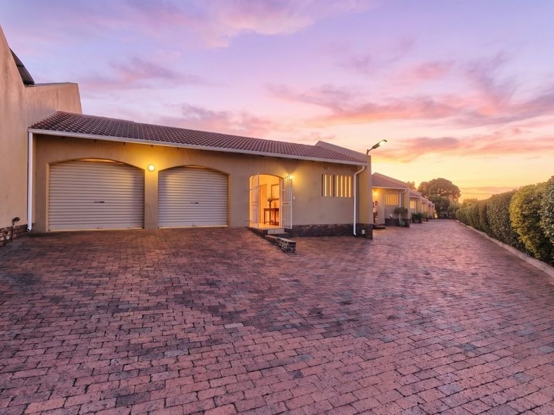 A well-maintained townhouse exterior featuring a double garage, brick-paved driveway, and secure entrance at sunset.