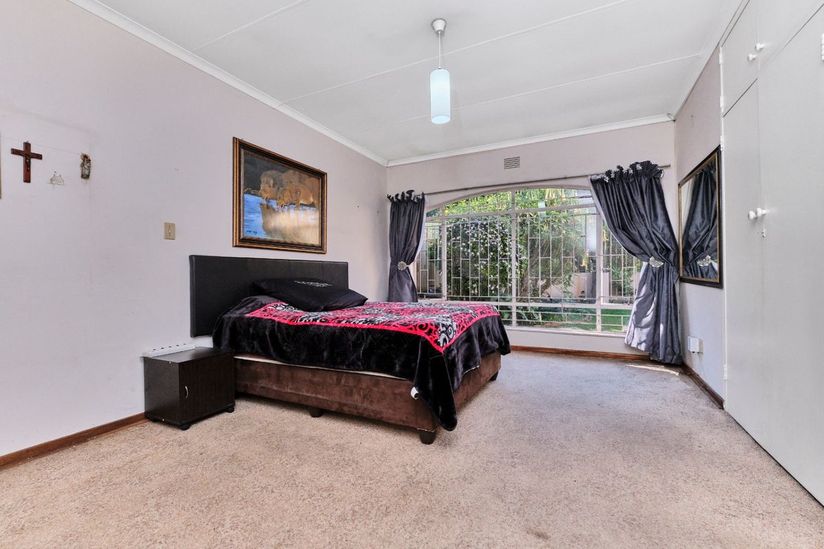 Spacious bedroom featuring built-in cupboards, carpeted flooring, and a large arched window with security bars overlooking the garden.