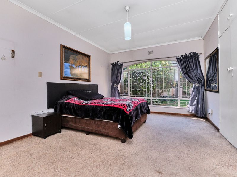 Spacious bedroom featuring built-in cupboards, carpeted flooring, and a large arched window with security bars overlooking the garden.