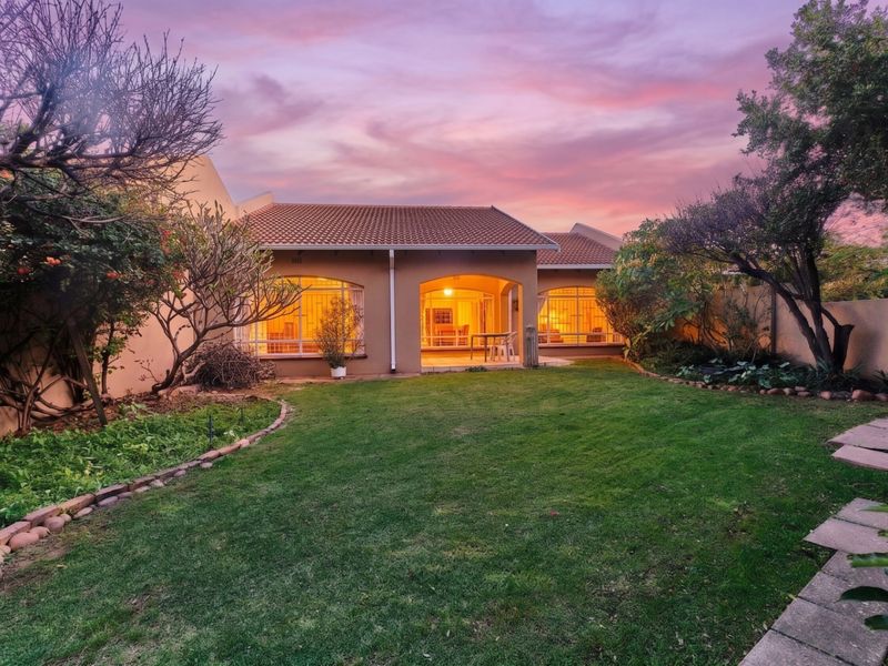 A well-maintained rear exterior view of the townhouse featuring a landscaped garden, paved walkway, and a covered patio area at sunset.