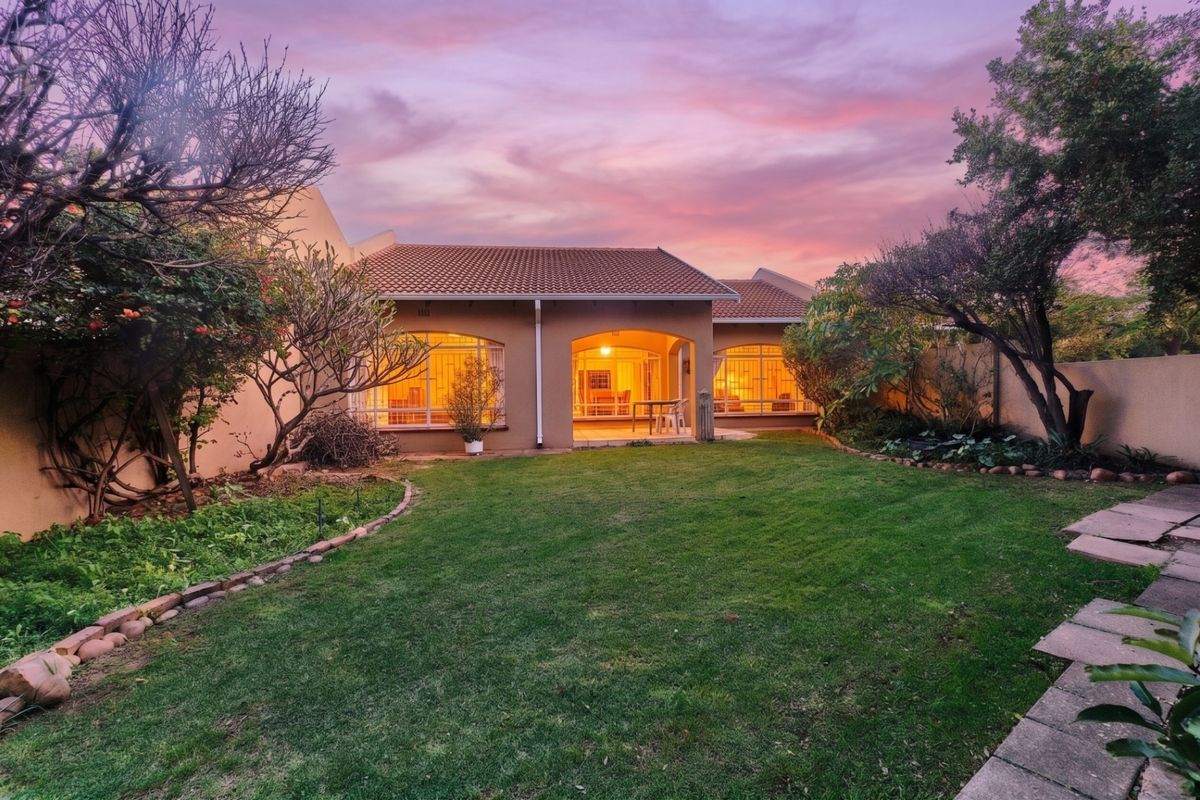 A well-maintained rear exterior view of the townhouse featuring a landscaped garden, paved walkway, and a covered patio area at sunset.