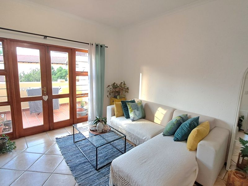 A bright living room featuring tiled flooring and large wooden framed glass double doors providing access to an outdoor patio area.