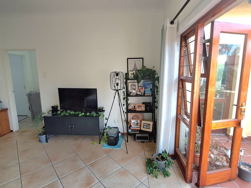 A living room area featuring tiled flooring and a wooden framed glass door providing access to an outdoor space.
